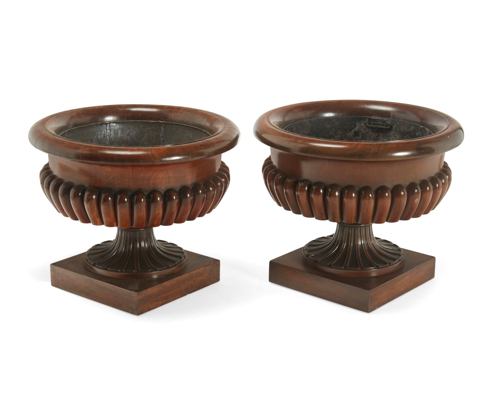 A matched pair of George IV carved mahogany wine coolers: A matched pair of George IV carved mahogany wine coolersOne early 19th century, one laterIn the manner of Gillows, each of circular form with gadrooned body and tapered fluted stem, on a square molded
