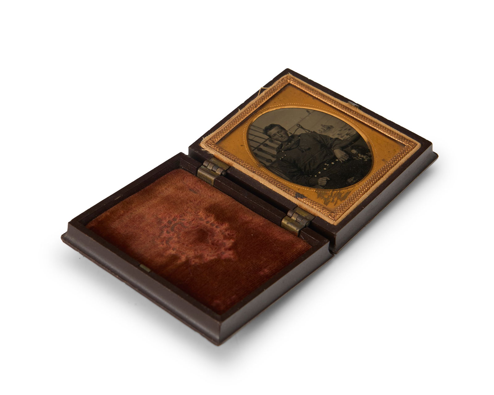 A 19th century tintype of a sailor: A 19th century tintype of a sailorA tintype featuring a portrait of a sailor in front of a faux boat background, with a chased gold-toned metal preserver within a burnt orange velvet-lined brown therm