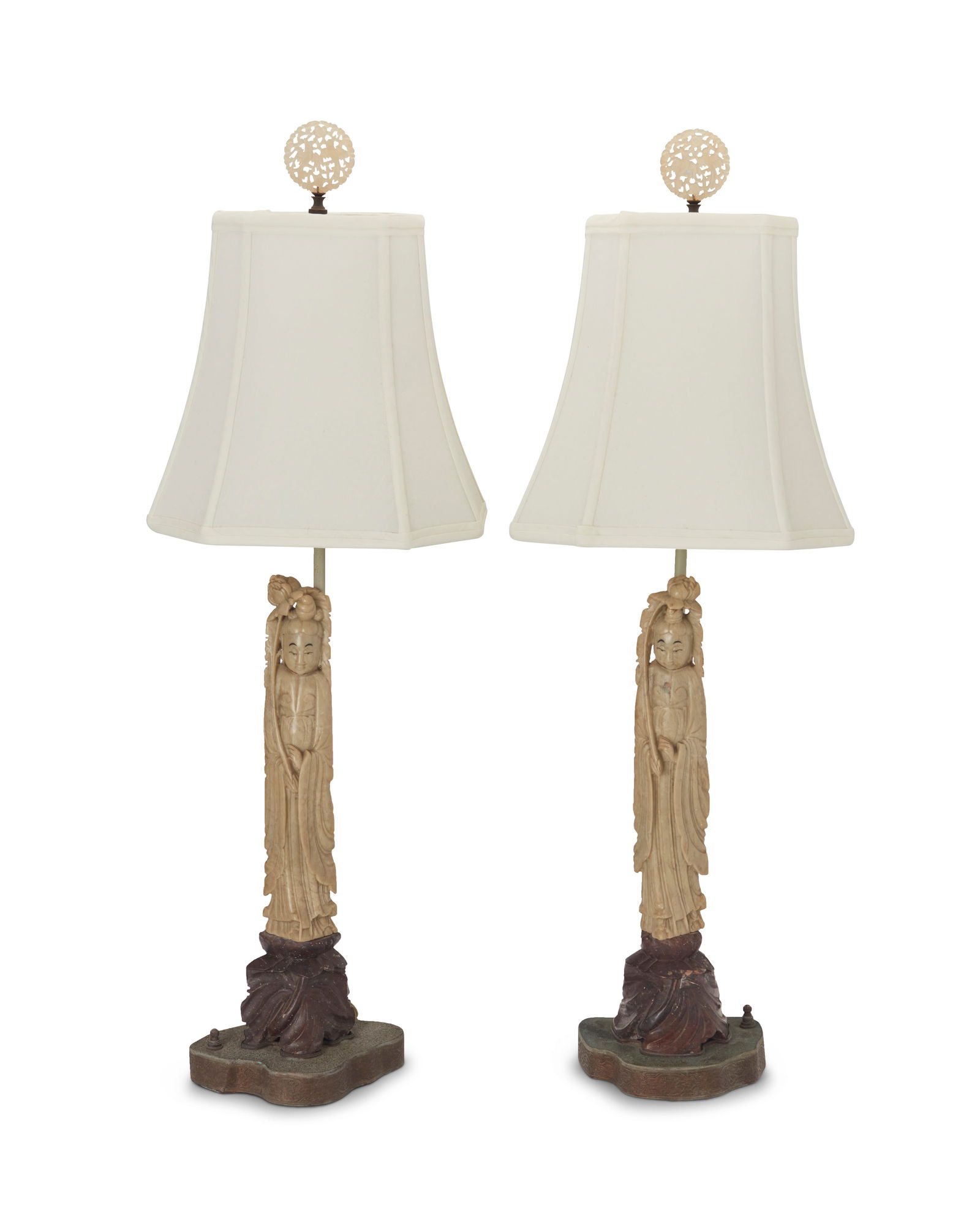 A pair of Asian carved hardstone lamps: A pair of Asian carved hardstone lampsMid-20th centuryThe single-light lamps, each with carved stone figural standard mounted on a brass base, surmounted by a fabric shade and a carved stone finial de