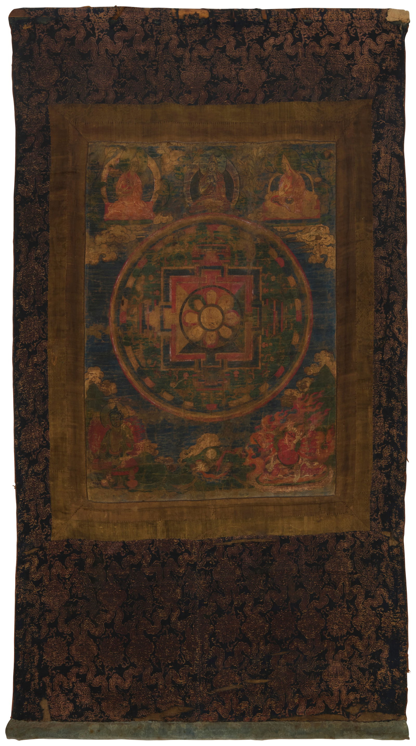 A 19th/20th century Tibetan thangka: A 19th/20th century Tibetan thangkaPainted panel depicting scenes of deities and Buddhist iconography in multicolored pigment on cotton, bordered by fabric brocade in navy, brown, and gold, as well as