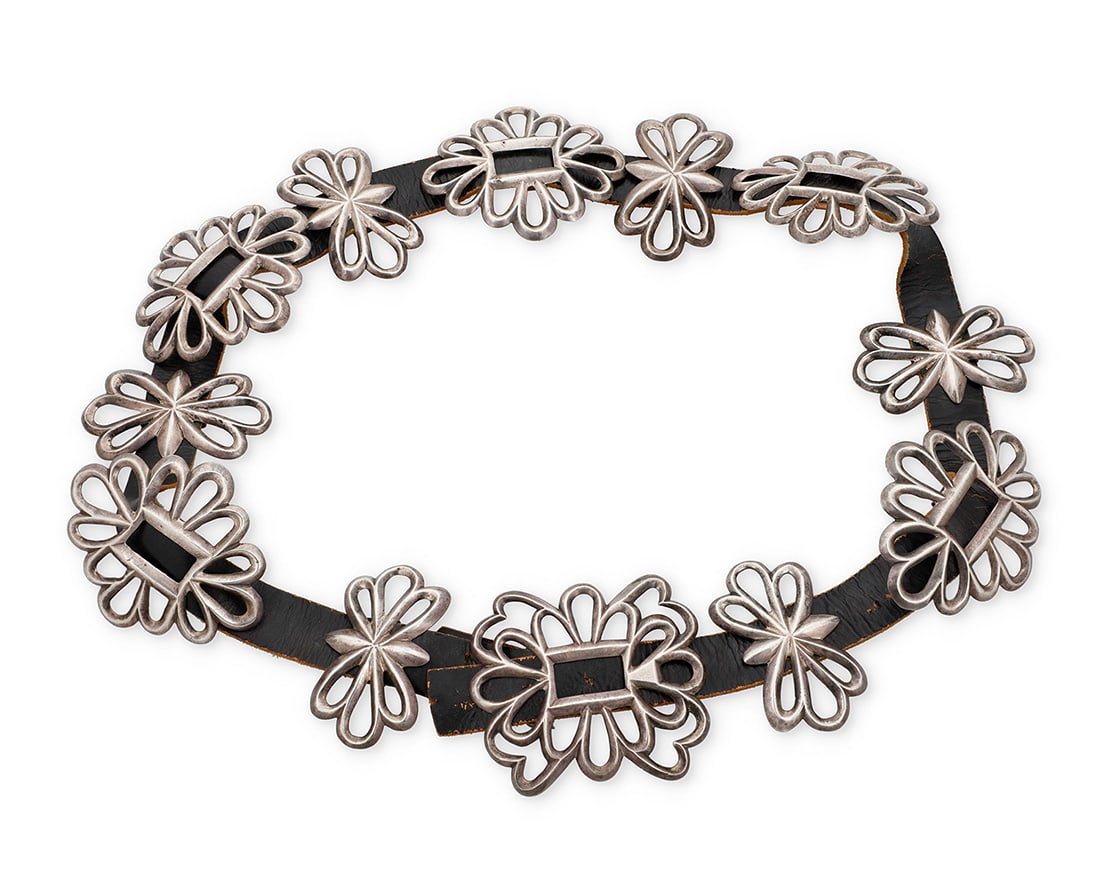 A Navajo cast sterling silver concho belt: A Navajo cast sterling silver concho beltEarly/mid-20th century, DineUnmarkedComprising a chunky filigree openwork buckle with five oval conchos and six narrow filigree spacers, each with copper backi
