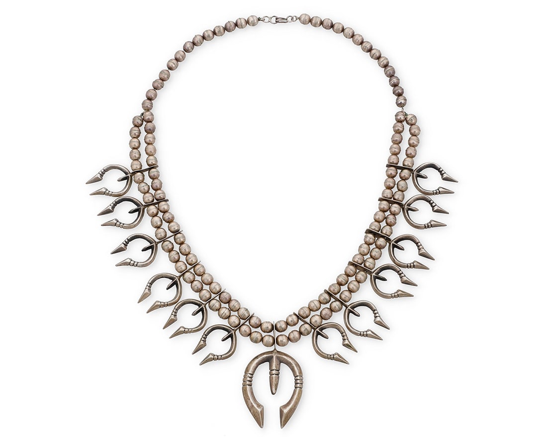 A Southwest cast sterling silver squash blossom necklace: A Southwest cast sterling silver squash blossom necklace Early/mid-20th century Unmarked A double strand of large silver beads suspending a central cast silver naja and twelve graduated cast silver