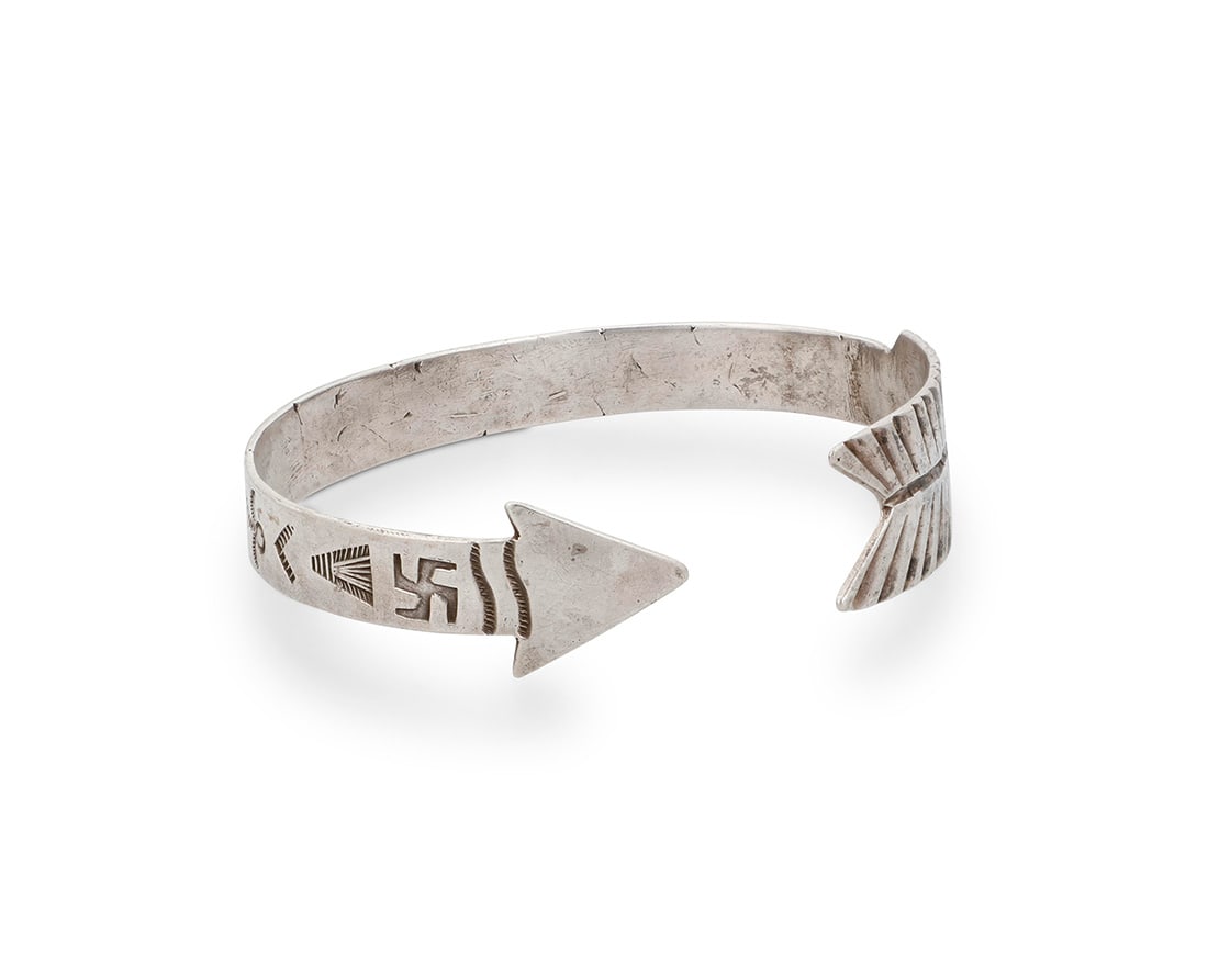 A Southwest sterling silver 'Arrow' cuff bracelet: A Southwest sterling silver 'Arrow' cuff bracelet Early/mid-20th century Unmarked An early narrow cuff with point and feather shaped terminals and stamp work including whirling logs and other