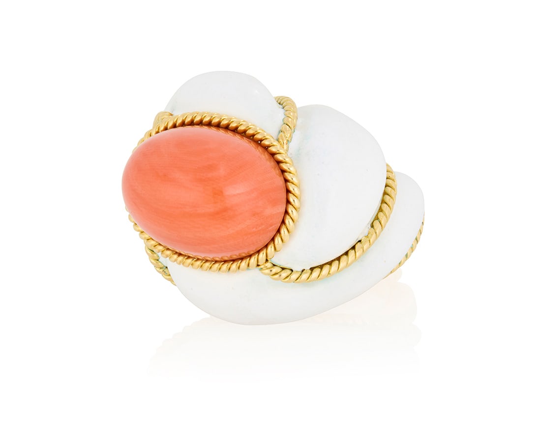 An 18K Gold, Coral and Enamel Ring: An 18K Gold, Coral and Enamel RingOf a domed design centering an oval coral cabochon set in twisting sections of white enamel and gold rope accentsSize: 6 1/237.1 gramsProvenance:The Estate of Jo