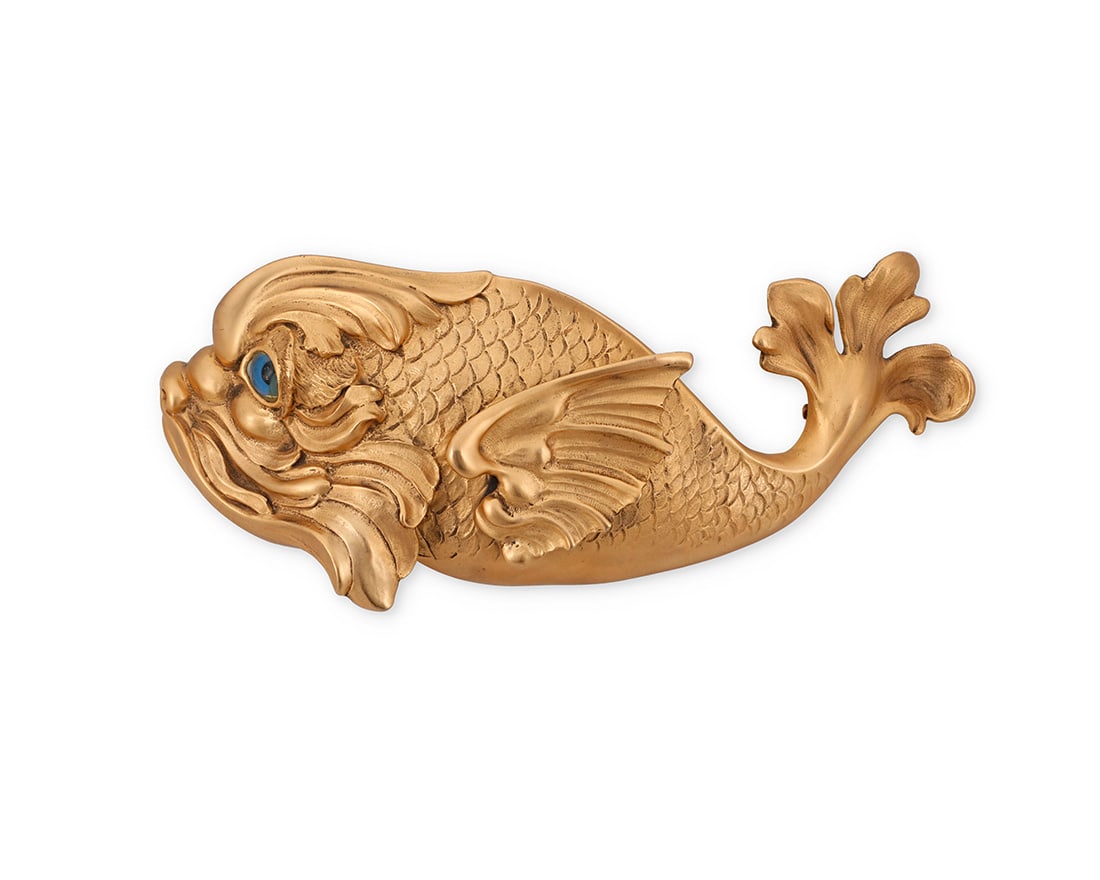 Christopher Ross: A Vintage Gold Tone Fish Belt Buckle: Christopher Ross: A Vintage Gold Tone Fish Belt BuckleCirca 1984A heavy cast gold-toned metal buckle featuring a sculptural Classical-style fish with inset blue glass eye and acanthus leaf tail, signe