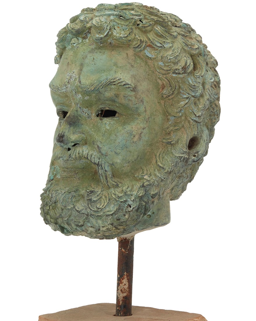 A Greek style bronze head: A Greek style bronze head20th centuryWith verdigris patination, raised on a metal rod issued from a concrete baseHead: 9.25" H x 7" W x 8.375" D; Overall: 17" H x 8.5" W Provenance:Collection of Stefa