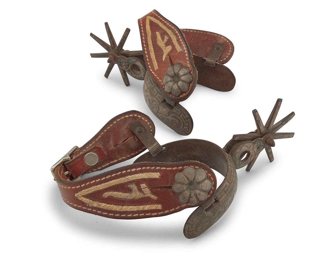 A pair of silver overlay spurs: A pair of silver overlay spurs 20th century The wrought iron spurs with inlaid silver bands and tracery motifs to outer heel band, shanks, outer strap buttons, and rowels, each spur with a circular