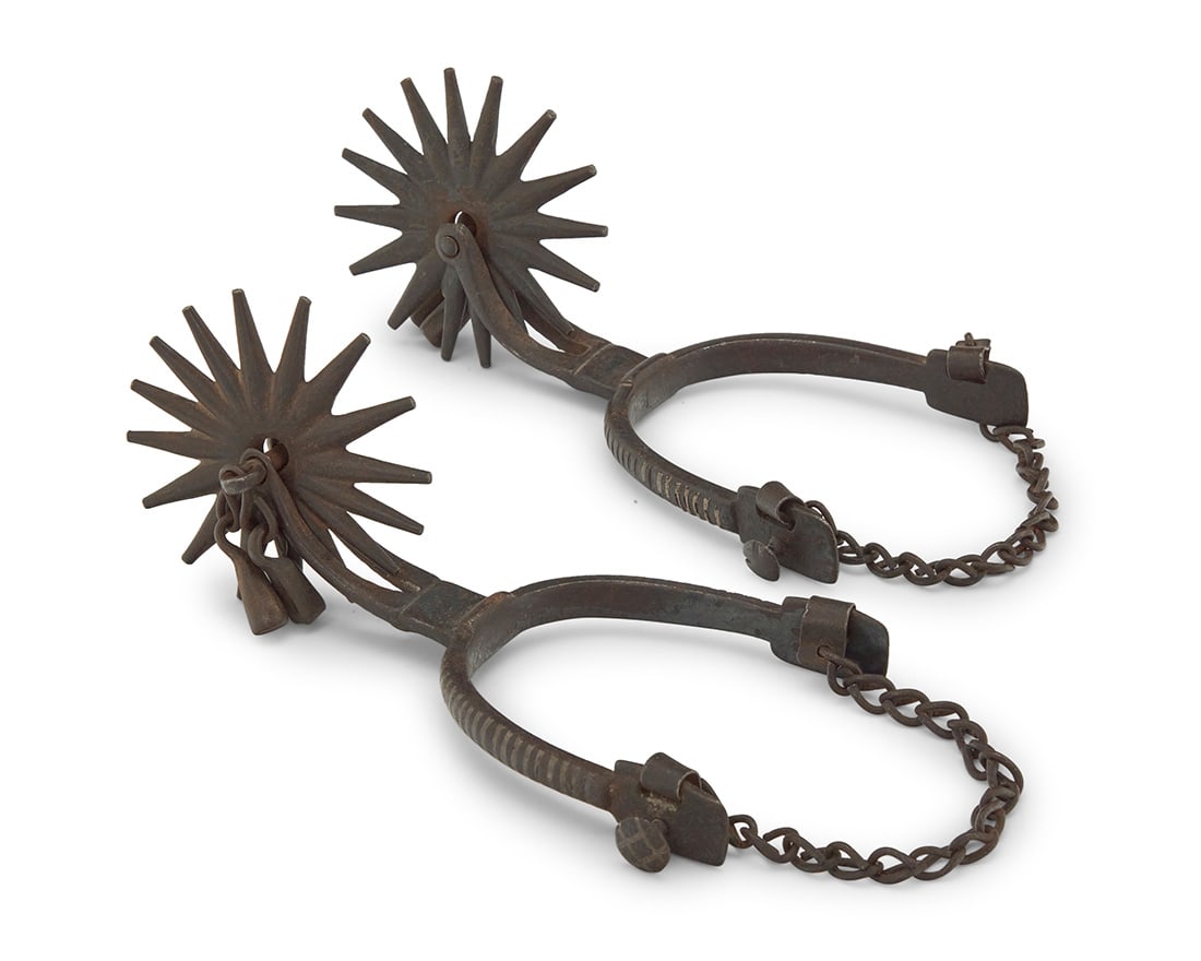 A pair of California vaquero style spurs: A pair of California vaquero style spurs 20th century The wrought iron spurs with narrow bands of silver inlaid to outer heel band and shanks, each with a split shank issuing a sixteen-point rowel