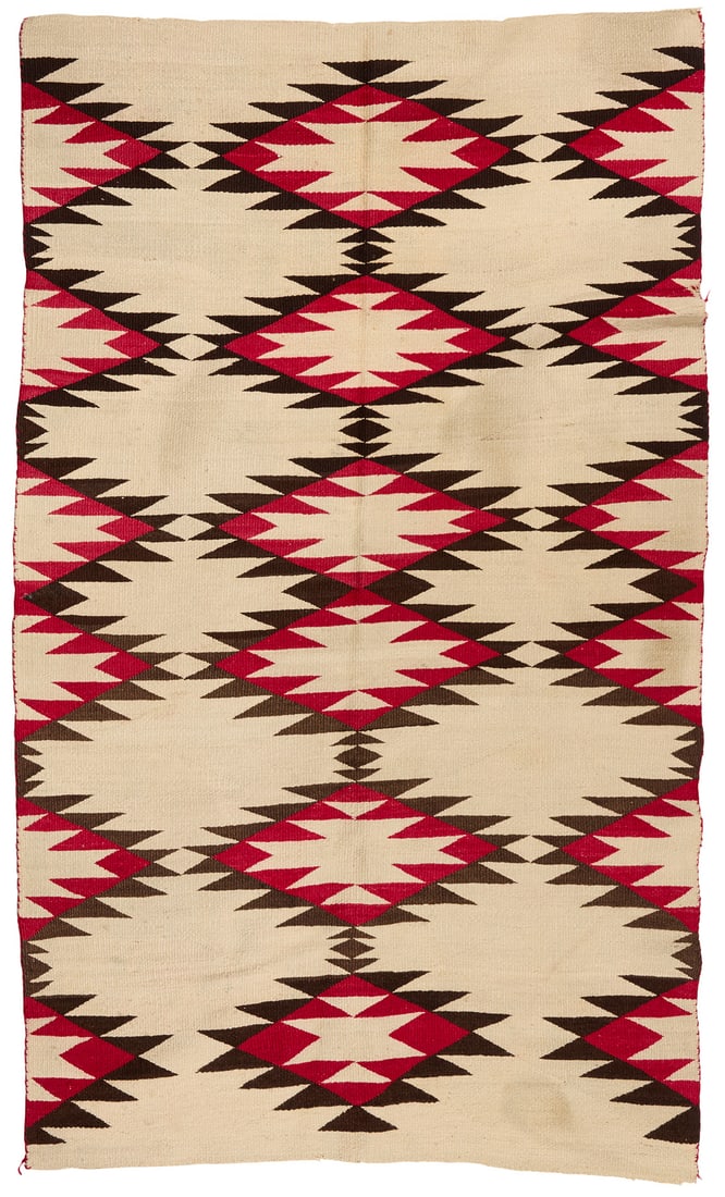 A Navajo regional rug: A Navajo regional rug Mid-20th century, Dine Woven in red, dark brown, and cream wool, with rows of stacked serrated diamonds 68" H x 40" W Provenance: Triton Museum of Art, Santa Clara, CA