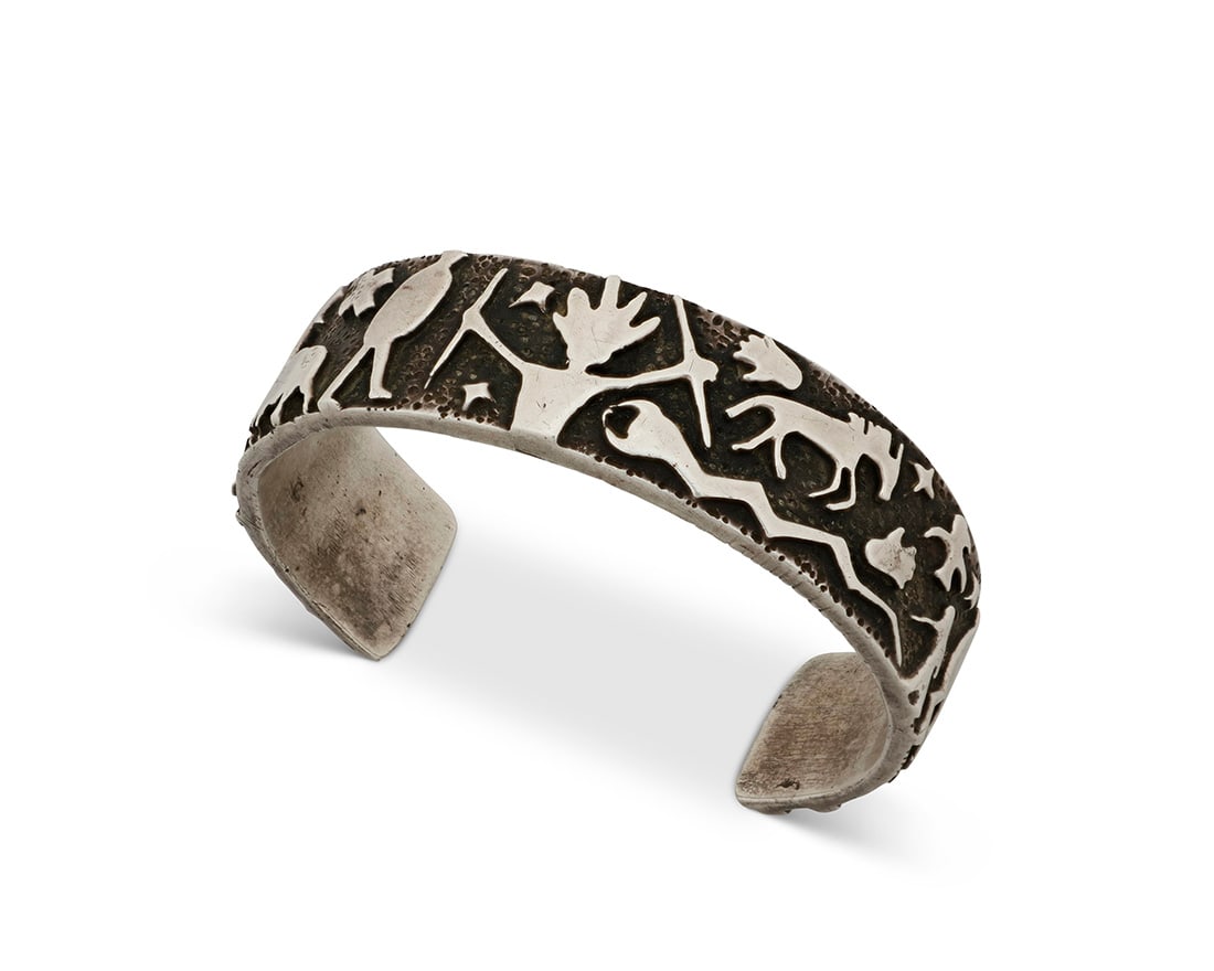 A Danny Romero sterling silver cuff bracelet: A Danny Romero sterling silver cuff bracelet Danny Romero (1954-2018; Yaqui/Spanish) Stamped: D R.MER. / FINE / [pictograph] A chunky sterling silver cuff with figural silver overlay featuring