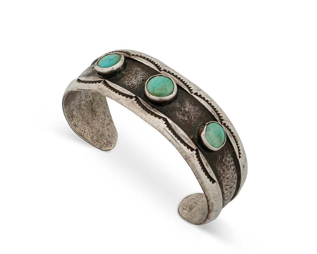 A Southwest sandcast ingot silver and turquoise cuff bracelet: A Southwest sandcast ingot silver and turquoise cuff bracelet Mid/late 20th century Stamped: E A chunky cuff with three set turquoise stones and stamped edge accents 6.25" total inner C x 0.875" H,
