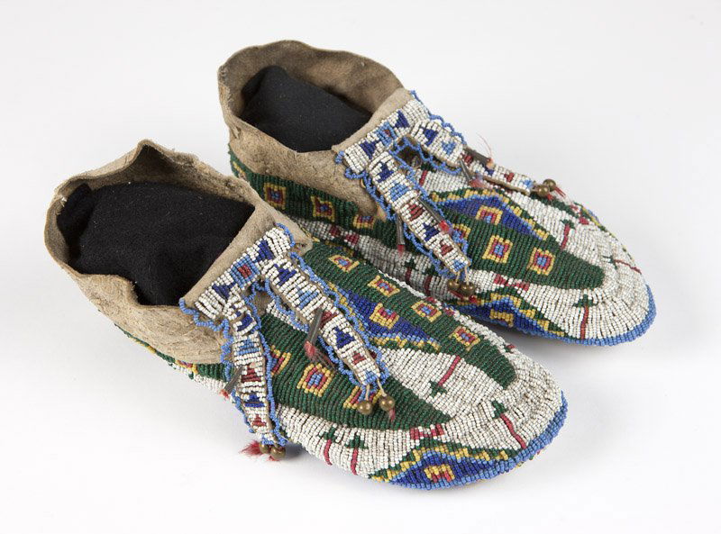 A pair of Plains Indian ceremonial moccasins: Late 19th century, the uppers and soles covered in a geometric pattern of white, dark blue, light blue, red, green and yellow beads, with bifurcated beaded tongues; 2 pcs, each 4'' H x 9.5'' W x 3.5''