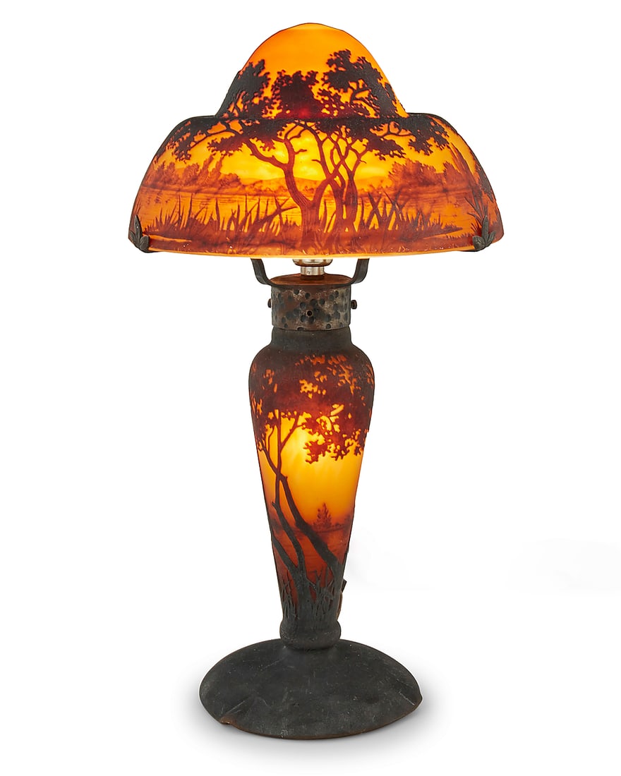 A Daum cameo glass landscape table lamp: A Daum cameo glass landscape table lamp Early 20th Century Signed: Daum Nancy [Croix de Lorraine] With two lights, one illuminating the base, the base and shade each decorated with a landscape scene, 