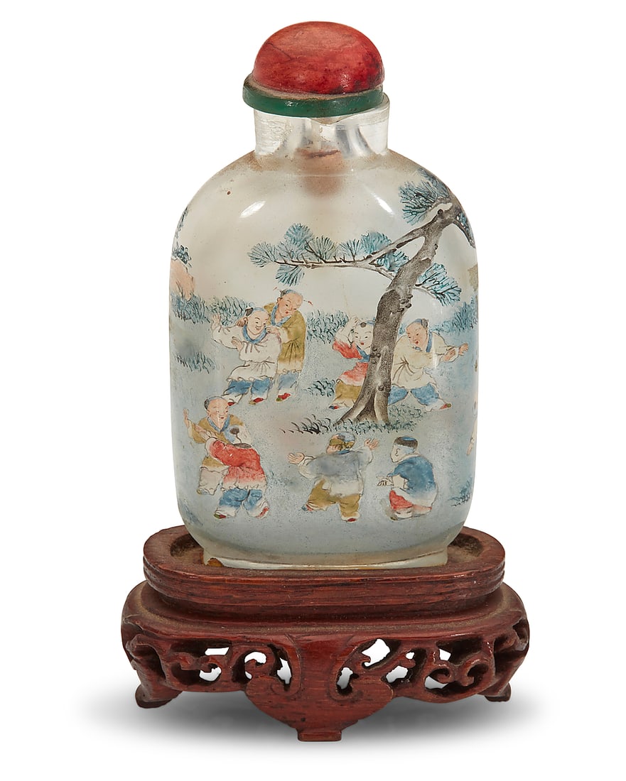A Chinese inside painted rock crystal 'One Hundred Boys' snuff bottle: A Chinese inside painted rock crystal 'One Hundred Boys' snuff bottle With cyclical date to 1903 Depicting boys at play beneath a tree, raised on a carved wood stand Bottle: 2.875" H x 1.5" W x 0.75" 