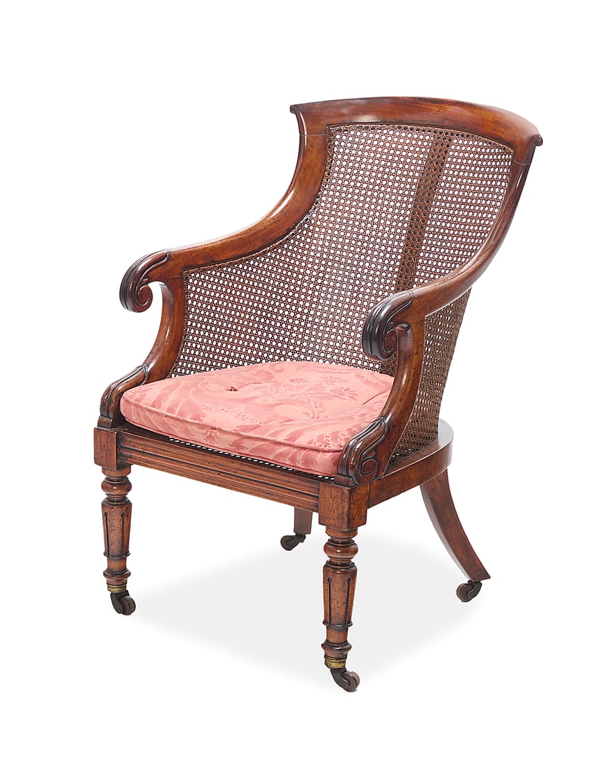 A William IV caned mahogany armchair: A William IV caned mahogany armchair Circa 1820 With caned seat and back, sloping armrests ending in scrolls, later upholstered seat cushion, on ring-turned legs raised on casters 37" H x 23" W x 30" 