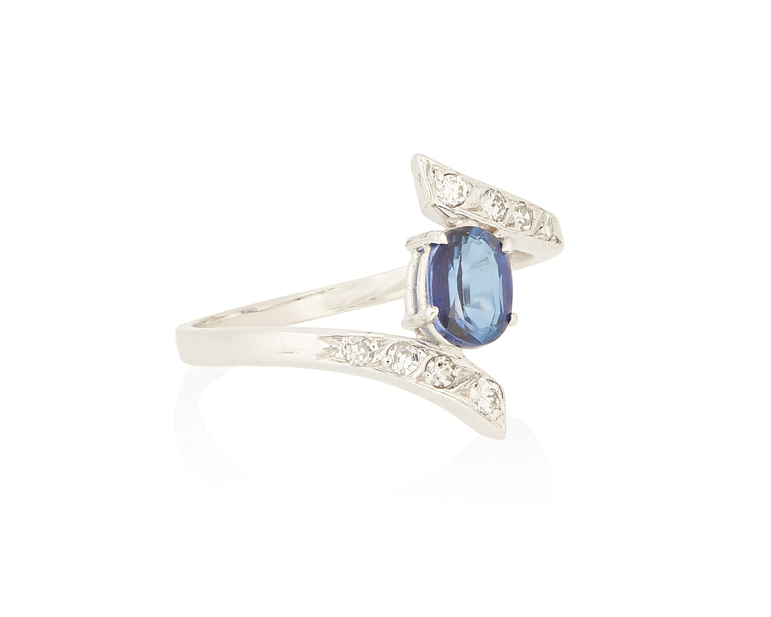 An 18K White Gold, Sapphire and Diamond Ring: An 18K White Gold, Sapphire and Diamond Ring Centering an oval sapphire weighing approximately 0.90 carat accented by round and single-cut diamonds set in a bypass design Size: 8 3/4 3.56 grams gross