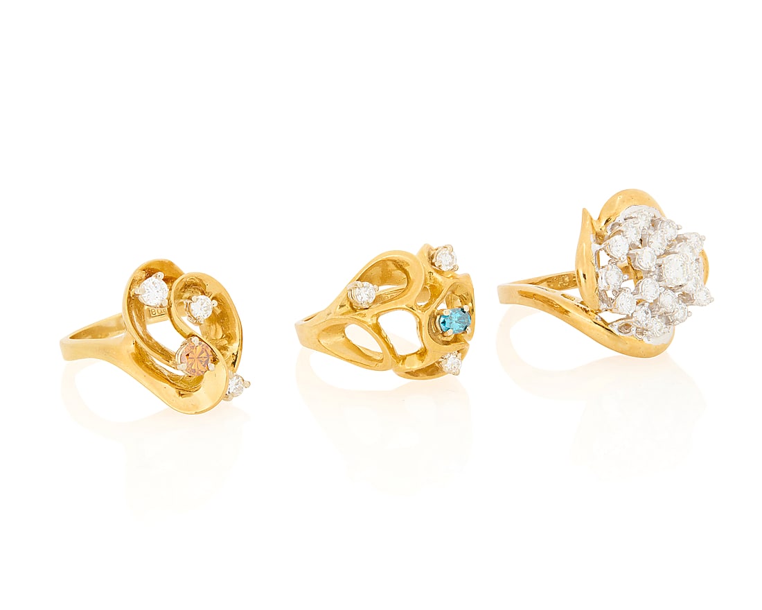 A Group of Three 18K Gold Rings: A Group of Three 18K Gold Rings Of swirling designs accented by round diamonds, an oval blue diamond and a round orange diamond 3 pieces Sizes: 6 1/2 27.3 grams gross