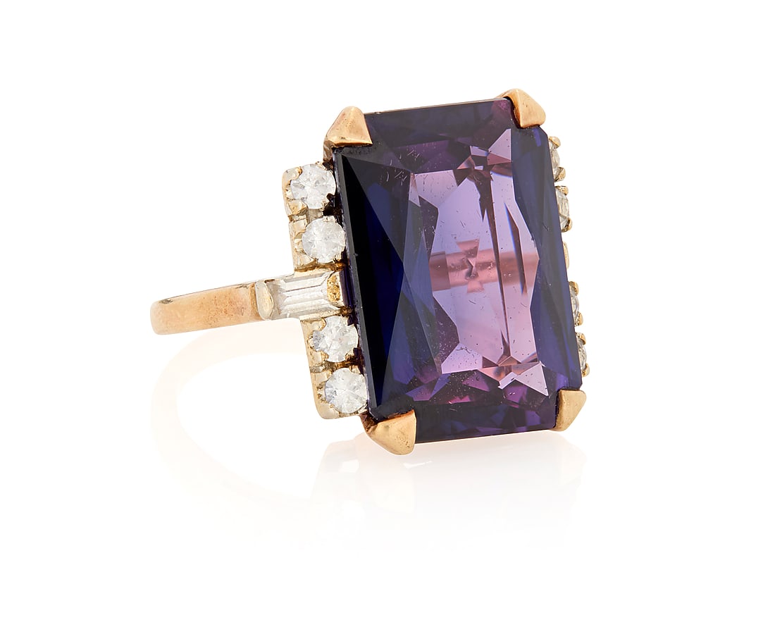 A 10K Gold and Synthetic Doublet Sapphire Ring: A 10K Gold and Synthetic Doublet Sapphire Ring Centering a mixed-cut synthetic purple doublet sapphire measuring approximately 17.80 x 13.00 x 6.90mm, accented by baguette and round near colorless