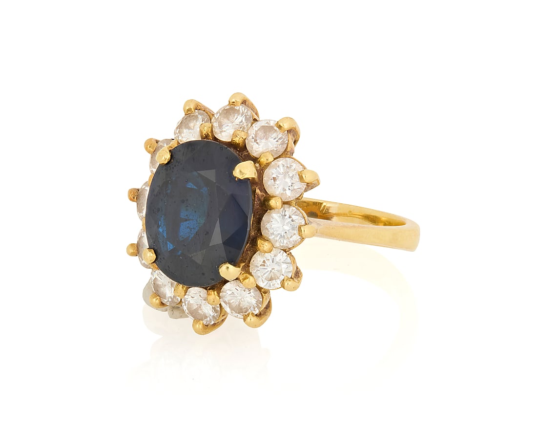 An 18K Gold, Sapphire and Diamond Ring: An 18K Gold, Sapphire and Diamond Ring Centering an oval sapphire measuring approximately 8.43 x 6.94 mm, encircled by round diamonds weighing approximately 0.84 carat Size: 2 1/2 4.1 grams gross Prop