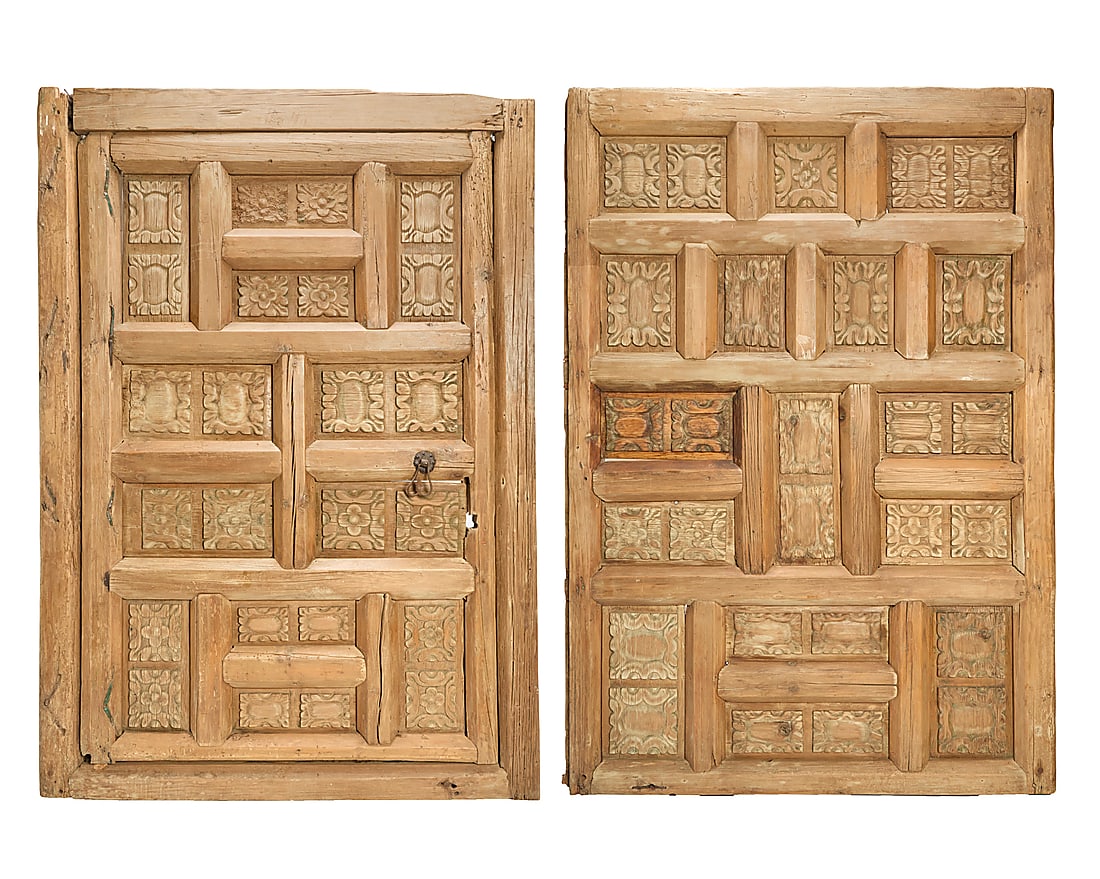A pair of Mexican carved wood doors: A pair of Mexican carved wood doors 19th century Each with recessed carved decorative panels, one mounted with a wrought-iron floral medallion pull 2 pieces Larger: 86.5" H x 61" W x 4" D; Smaller: 85