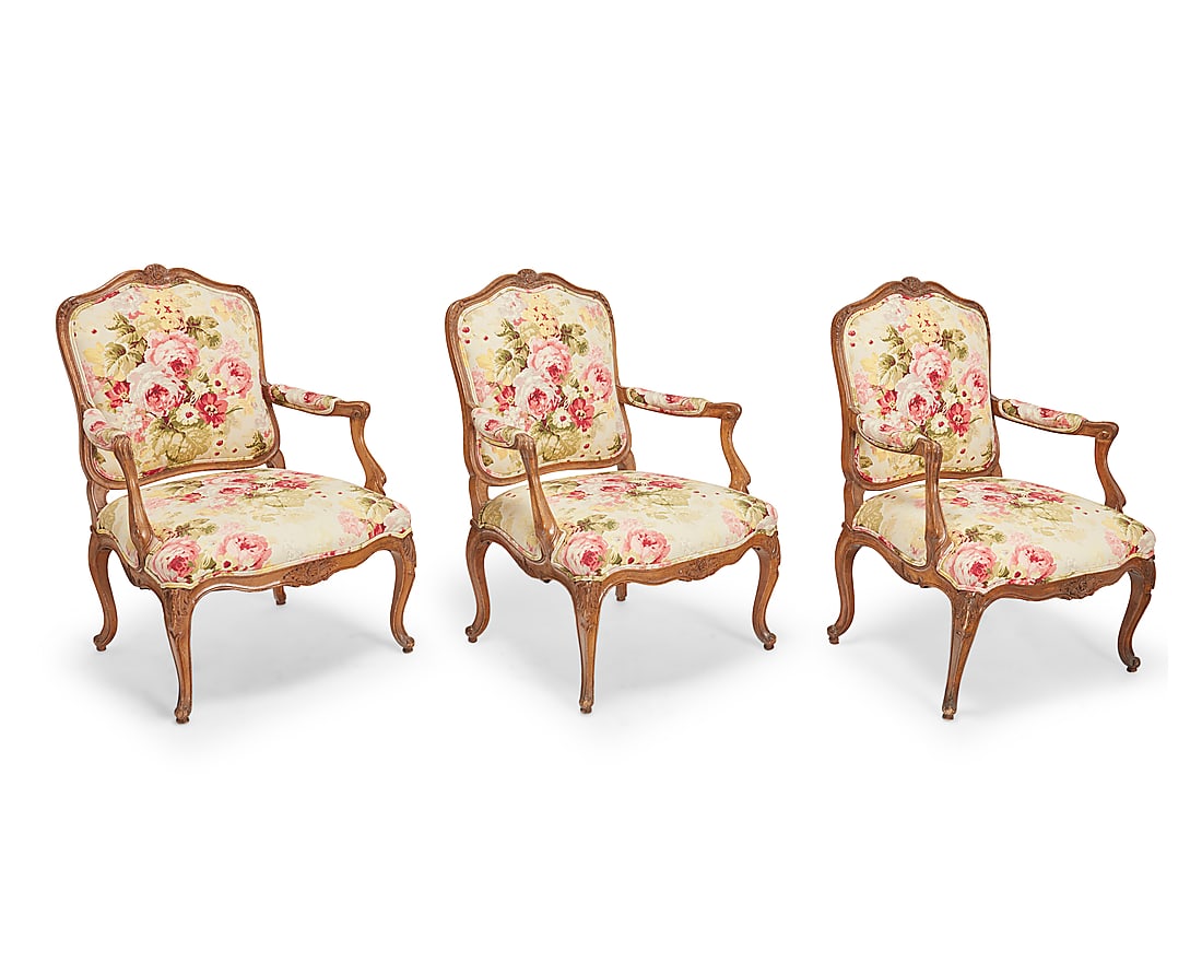 A set of three Louis XV carved walnut fauteuils Mid-late 18th century with later elements Each: A set of three Louis XV carved walnut fauteuils Mid-late 18th century with later elements Each wood armchair with carved foliate accents and scroll armrest terminals, the seatback, seat cushion, and a