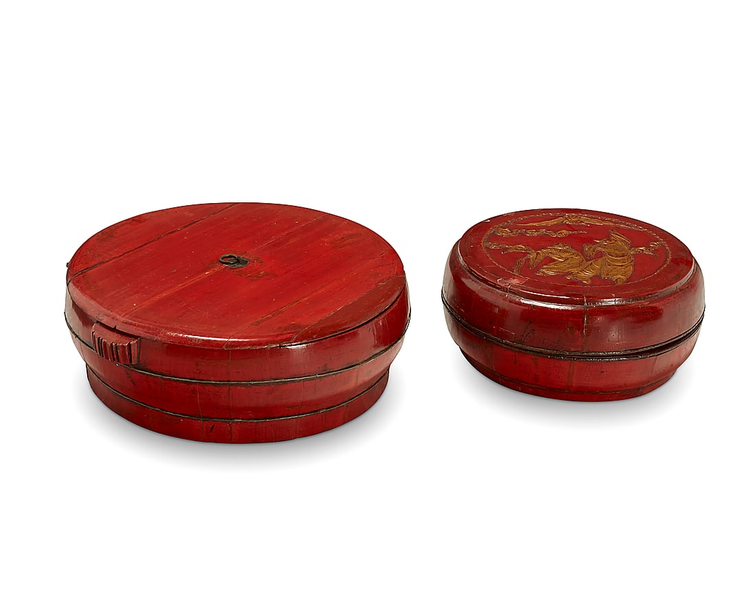 Two Chinese red lacquered wood storage containers 20th century Comprising one with a metal ring: Two Chinese red lacquered wood storage containers 20th century Comprising one with a metal ring handle and another decorated with carved and gilt-accented figures 2 pieces Figures: 8" H x 10" Dia.; Ha