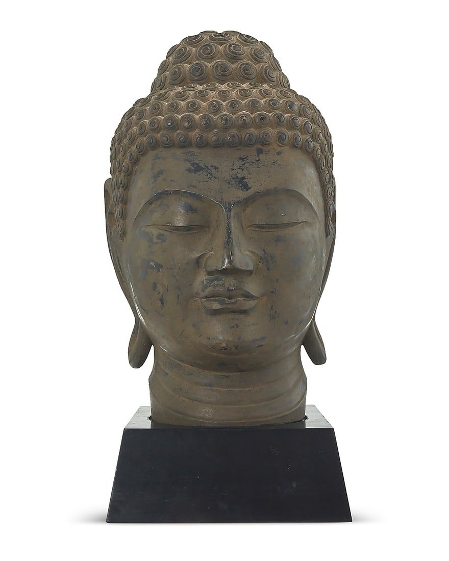 An Asian style carved wood head of Buddha 20th/21st century Antiqued enameled hardwood raised on a: An Asian style carved wood head of Buddha 20th/21st century Antiqued enameled hardwood raised on a wood base Head: 9.25" H x 11.5" W x 13.5" D; Base: 4.25" H x 11" W x 12" D