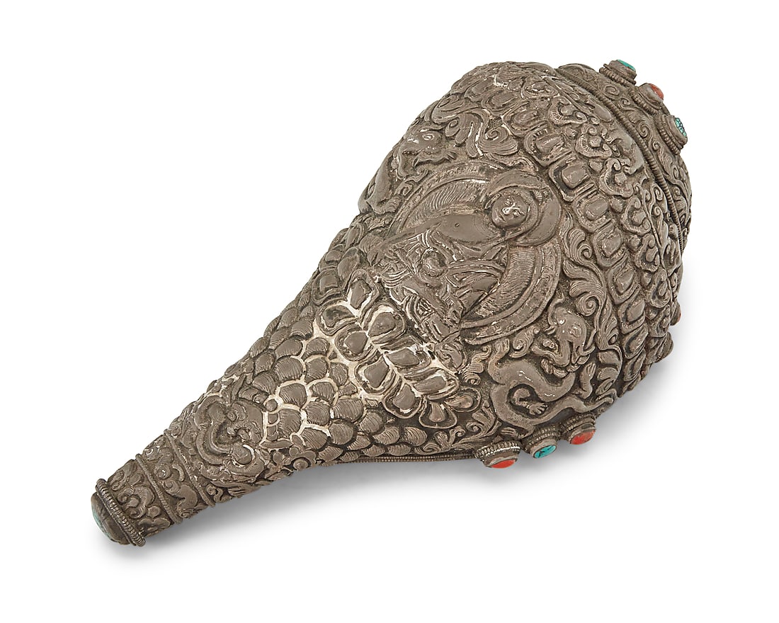 A Tibetan Buddhist sterling silver clad conch shell 19th/20th century XRF tested for sterling Set: A Tibetan Buddhist sterling silver clad conch shell 19th/20th century XRF tested for sterling Set with turquoise and coral accents, depicting a central Buddha figure with dragons, animals, and mythica