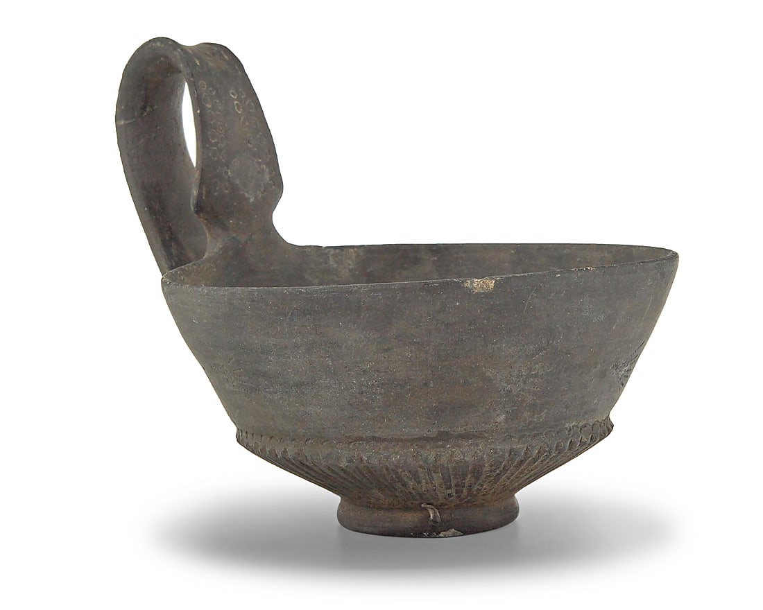 An Etruscan Bucchero pottery kyathos: An Etruscan Bucchero pottery kyathos 7th-5th century BCE or later The drinking cup with incised accents to handle and body 5" H x 5.375" W x 6.625" D