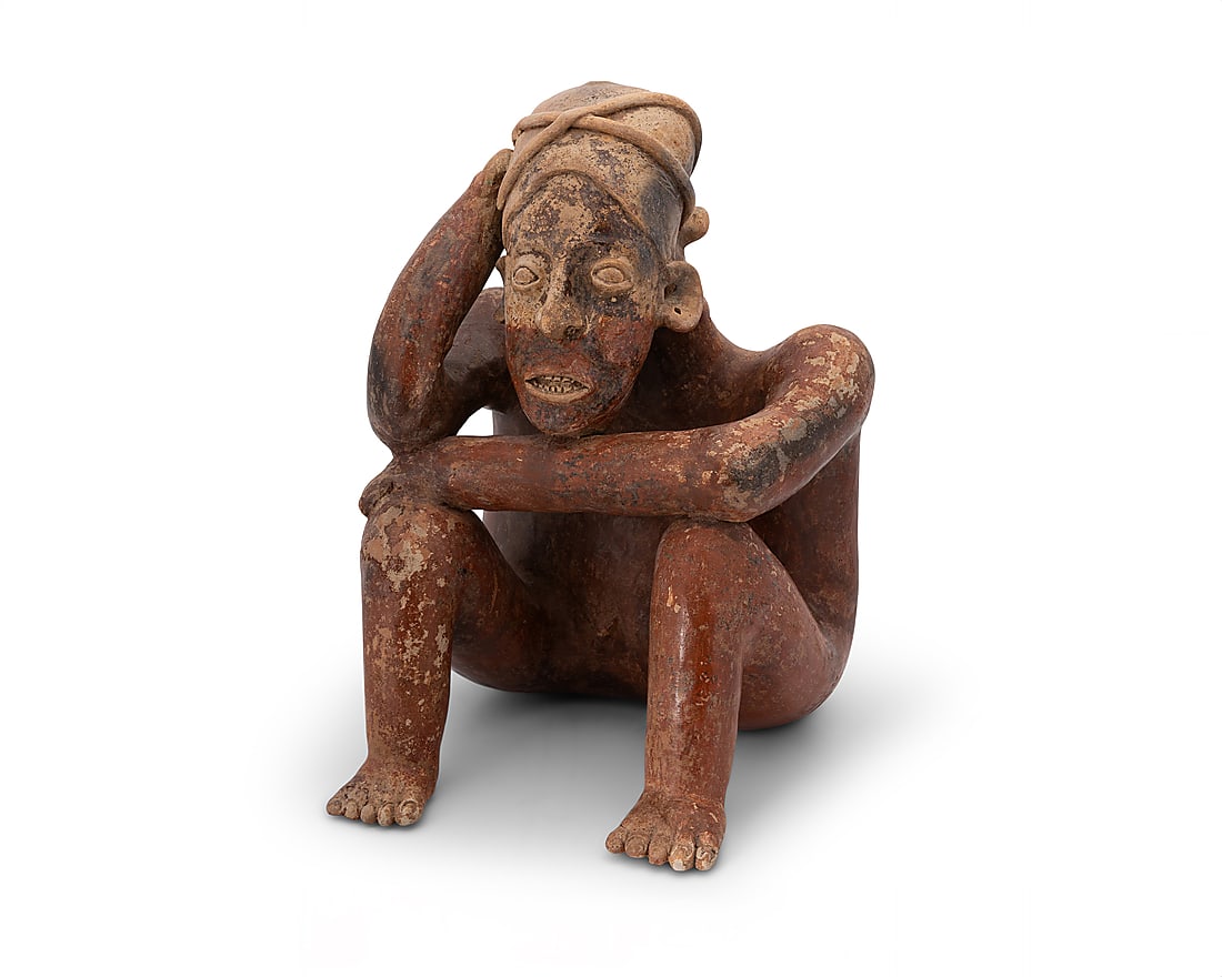 A Pre Columbian pottery figure: A Pre Columbian pottery figure Pre-100 CE; Jalisco, West Mexico The terracotta ceramic hollow-body figure depicted seated in a pensive pose, with a headpiece and incised facial features 13.75" H x