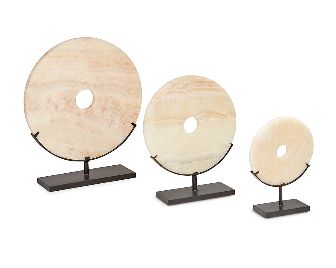 Three onyx disc table items: Three onyx disc table items Early 21st century Comprising three circular cream onyx discs in graduated sizes, each with hole at center and raised on a black enameled metal stand 3 pieces Largest
