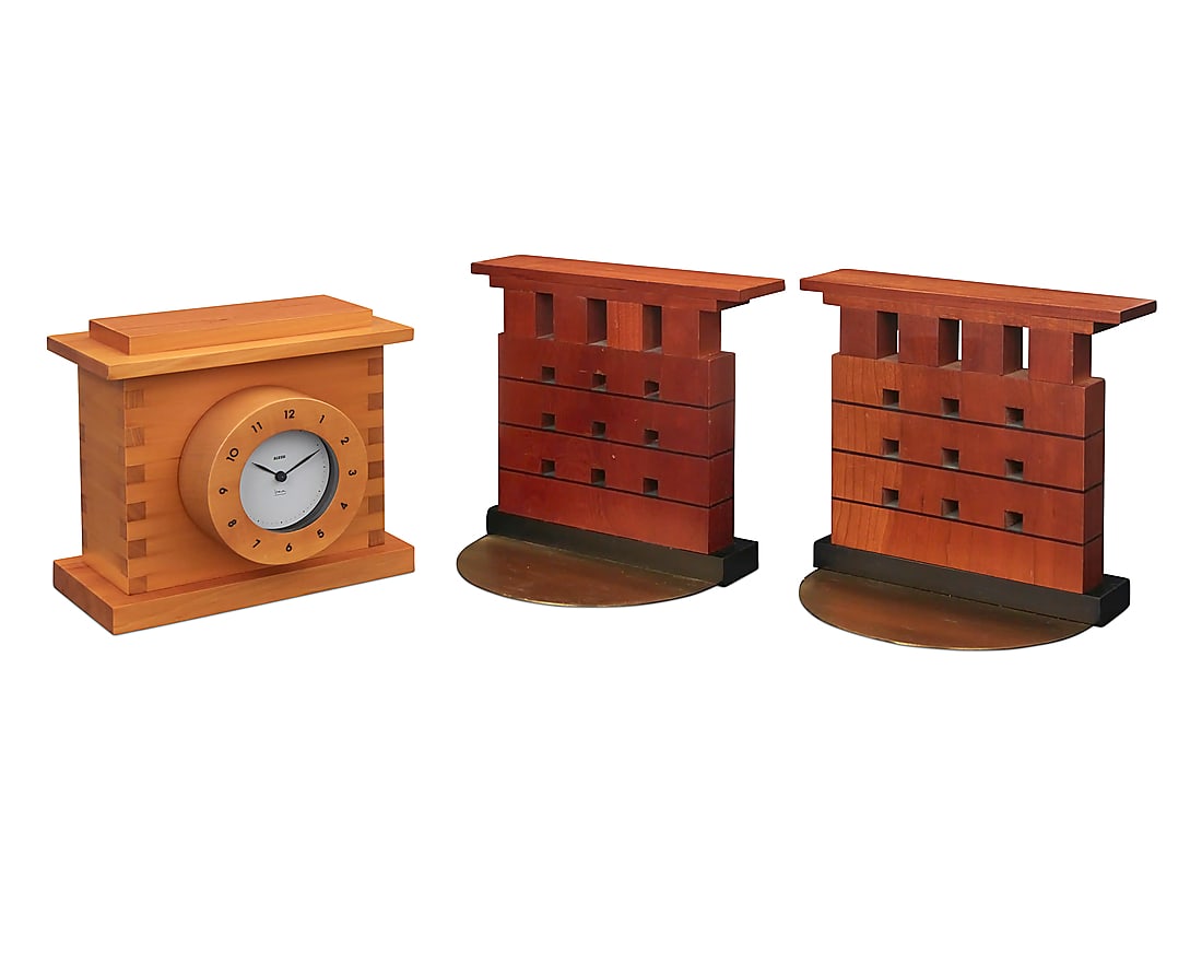 Michael Graves (1934-2015), A table clock for Alessi and pair of bookends, 1990s: Michael Graves (1934-2015) A table clock for Alessi and pair of bookends, 1990s Clock lid impressed: ALESSI / ITALY / DESIGN MICHAEL GRAVES; dial with printed signature: Graves Each bookend maple, ebo