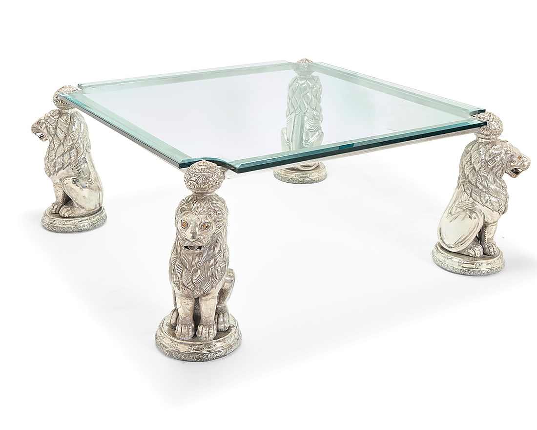 A silvered metal and glass coffee table: A silvered metal and glass coffee table 20th century The beveled glass set on a silver-toned metal frame with lion-form supports with glass eyes Base: 22" H x 49" W x 49" D; Glass: 0.625" H x 43" W x