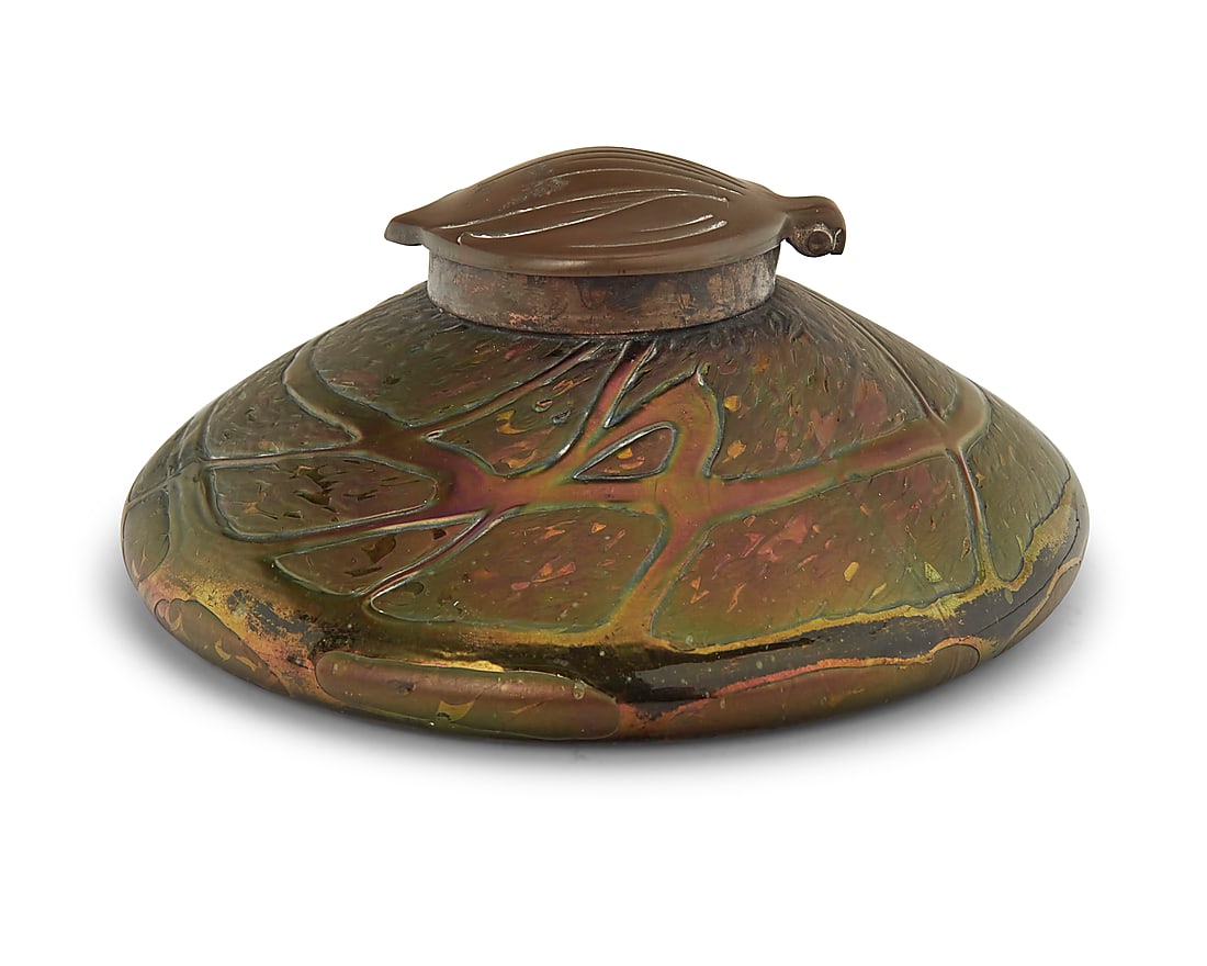 An Art Nouveau bronze and art glass inkwell: An Art Nouveau bronze and art glass inkwell Late 19th/early 20th century Appears unmarked Possibly Loetz, with iridescent glass and hinged foliate-form bronze hinged lid opening to reveal a glass inkw