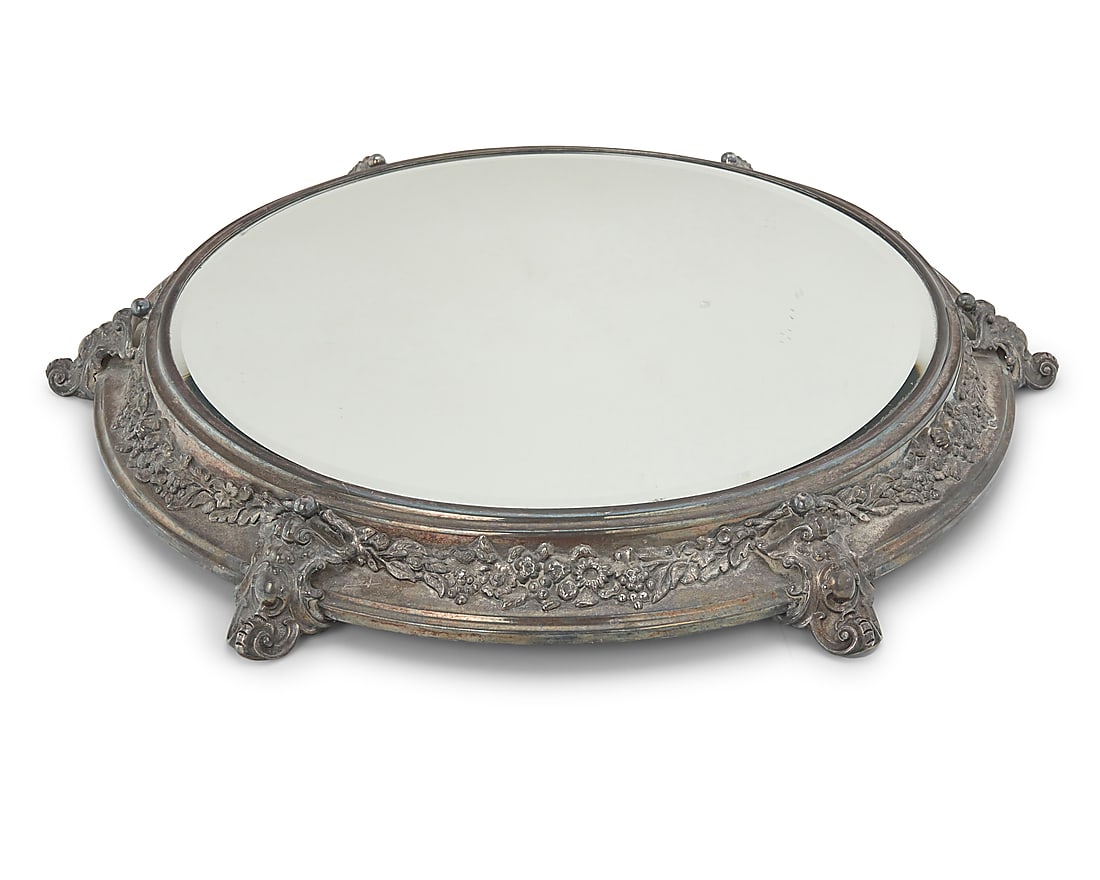 A Continental silver plated mirrored plateau: A Continental silver plated mirrored plateau Early 20th century With floral garlands, raised on scrolling cartouche feet Height 2 in., diameter 19 3/4 in.; diameter of glass 14 1/2 in.