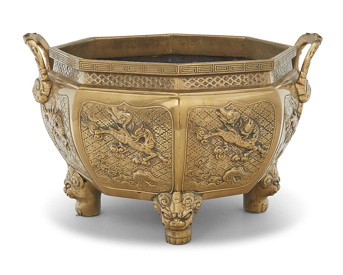 A Chinese brass octagonal jardiniere: A Chinese brass octagonal jardiniere 20th century Unmarked With opposed handles and guardian lions in relief, raised on lion-form feet Height 10 in., width 15 3/4 in., depth 14 in.