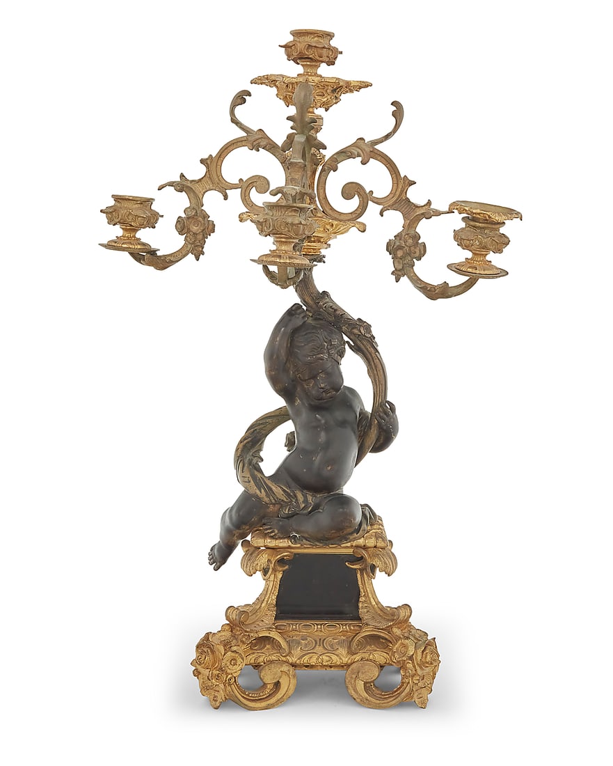 A French parcel gilt bronze figural candelabrum: A French parcel gilt bronze figural candelabrum Late 19th/early 20th century Each unmarked The putti-form standard issuing four lights, raised on an ornate scrolling foliate-form base Height 20 1/4 in
