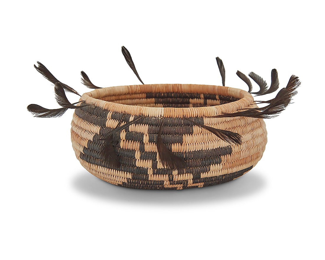 A Pomo gift basket: A Pomo gift basket Mid/late 20th century; Northern California The coiled small oval bowl with a diagonal stepped zigzag motif to each side and quail top knot feathers to the rim Height 2 in., width 4