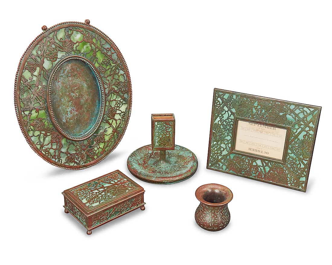 Five Tiffany Studios bronze and Favrile glass 'Grape Leaf' desk items: Five Tiffany Studios bronze and Favrile glass 'Grape Leaf' desk items Early 20th century Verdigris patinated, comprising an oval easel-back picture frame, an easel-back calendar holder with incomplete