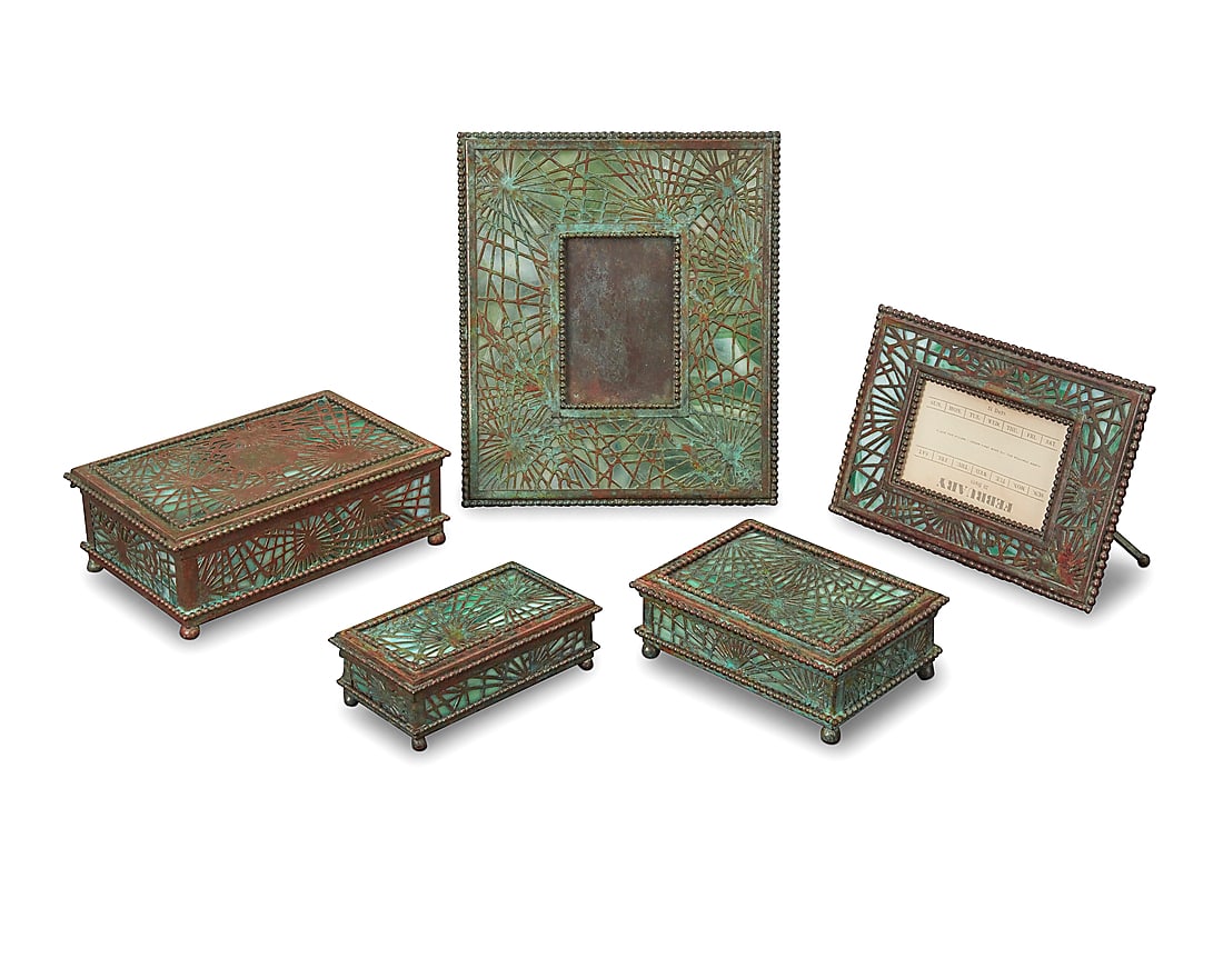 Five Tiffany Studios bronze and Favrile glass 'Pine Needle' desk items: Five Tiffany Studios bronze and Favrile glass 'Pine Needle' desk items Early 20th century Verdigris patinated, comprising two lidded boxes, a stamp box, an easel-back picture frame, and an easel-back 