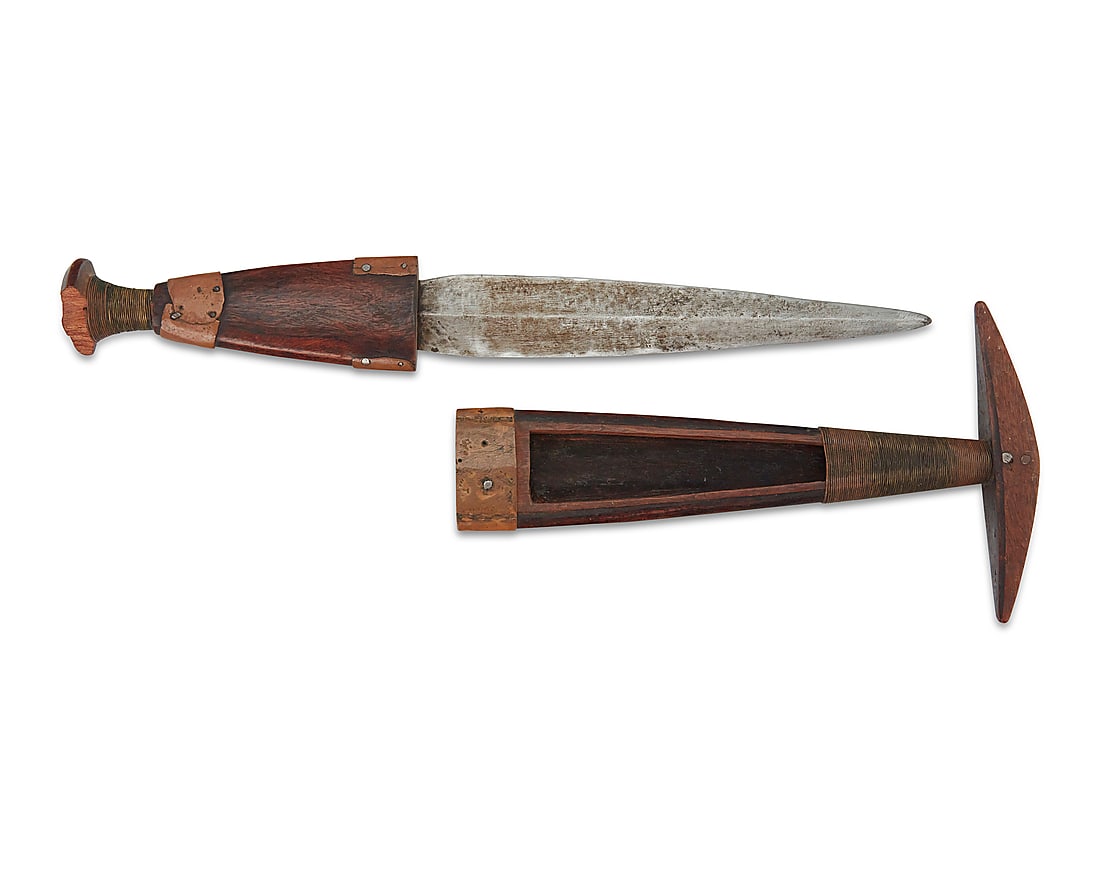 An Ovambo dagger with sheath: An Ovambo dagger with sheath Late 19th/early 20th century; Angola/Namibia Each in carved dark wood with copper and wrapped wire accents, featuring a tapered ridged metal blade set in a carved wood han