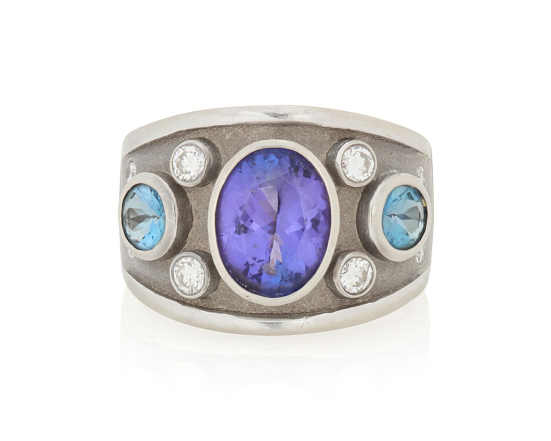 An 14K White Gold, Tanzanite and Diamond Ring Centering an oval tanzanite weighing approximately: An 14K White Gold, Tanzanite and Diamond Ring Centering an oval tanzanite weighing approximately 3.10 carats, flanked by two round blue topaz and ten round diamonds, signed CGJ Size: 8 13.9 grams gros