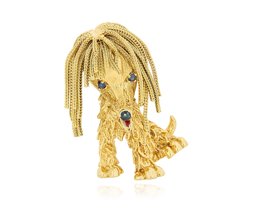 An 18K Gold and Enamel Brooch Of a long-haired dog design featuring dangling braided chain, two: An 18K Gold and Enamel Brooch Of a long-haired dog design featuring dangling braided chain, two round sapphire eyes and an enamel tongue and nose Measures: 1 1/2 x 1 in. 20.3 grams gross