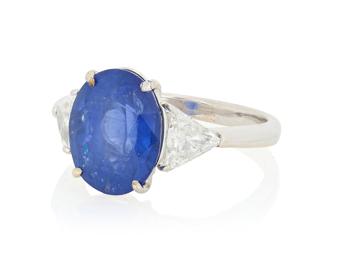 An 18K White Gold, Sapphire and Diamond Ring Centering an oval sapphire weighing approximately: An 18K White Gold, Sapphire and Diamond Ring Centering an oval sapphire weighing approximately 6.10 carats flanked by two triangular-cut diamonds weighing approximately 0.90 carats size: 6 5.3 grams g