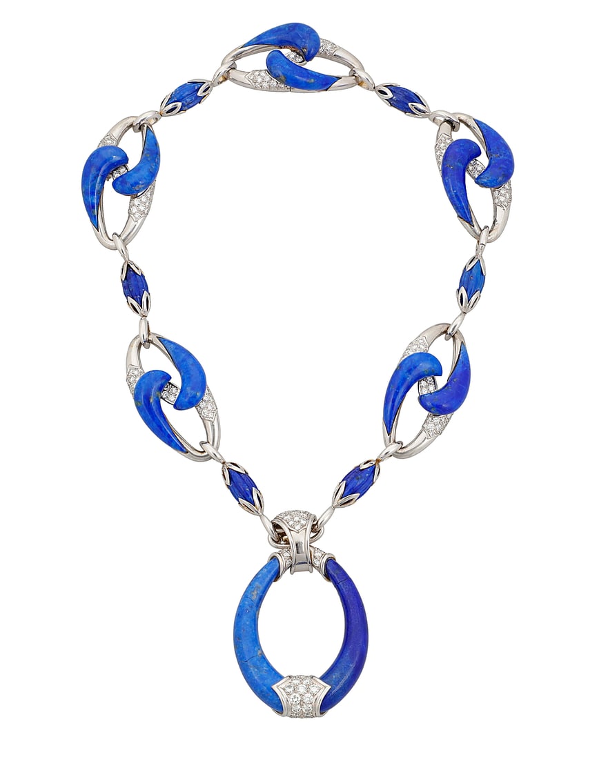 An 18K White Gold, Lapis Lazuli and Diamond Necklace Including a chain featuring swirling carved: An 18K White Gold, Lapis Lazuli and Diamond Necklace Including a chain featuring swirling carved elements of lapis lazuli contrasted by round diamonds, suspending a central pendant including carved gr