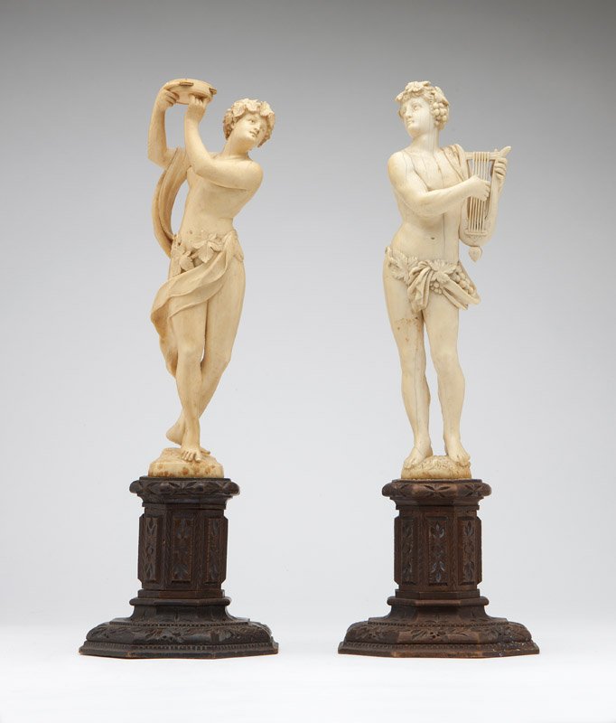 A pair of Continental carved ivory statues: Second half 19th century, each depicting a classical figure of a musician, one plucking a lyre, the other tapping a tambourine, each on an integral base, mounted to an octagonal carved wooden plinth, 