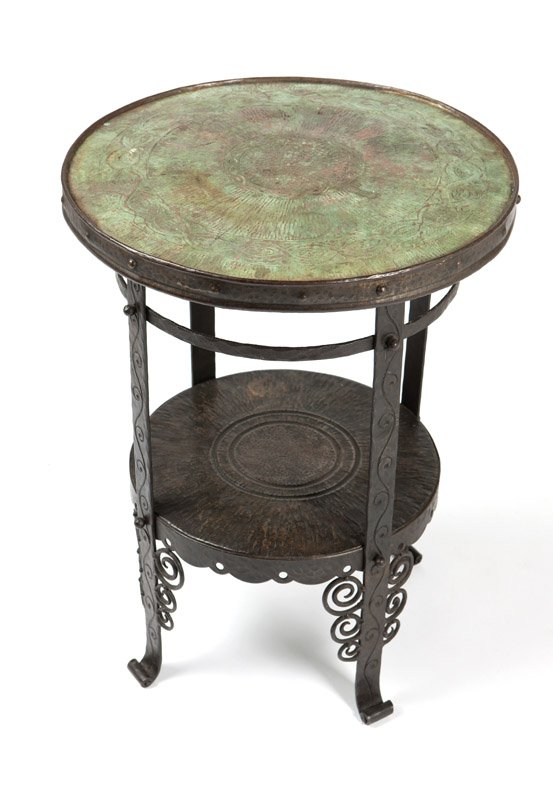 A forged iron & copper Arts & Crafts lamp table: Circa 1910, apparently unsigned, possibly by German maker Coberg, the inset circular top decorated with patterned bands, joined to a shelf with a pierced apron by four flat patterned legs with curlicu