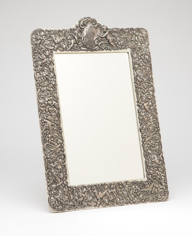 A Dominick & Haff sterling silver table mirror: Early 20th century, with maker's mark and further marked ''Sterling'' and ''158'', the rectangular plate within a pierced surround decorated with birds, scrolling foliage and flowers, surmounted by a 