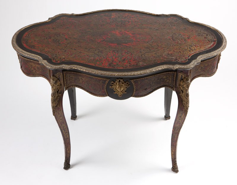 A gilt bronze-mounted 'Boulle' marquetry center table: Late 19th century, of cut-brass-inlaid faux tortoiseshell and ebonized wood, decorated overall with scrolled arabesques, the serpentine oval-shaped top centering a medallion of a warrior driving a cha