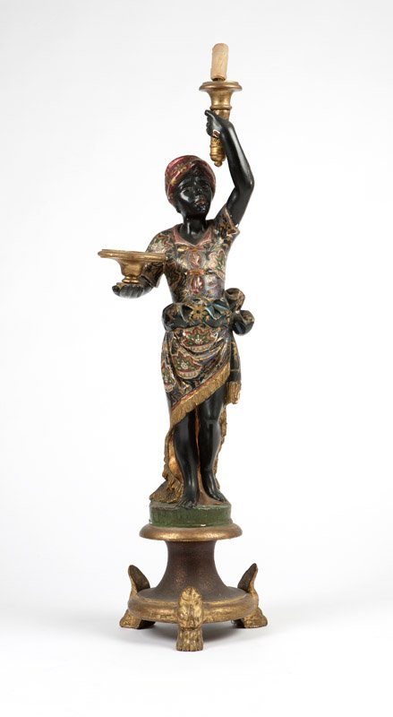 A polychromed carved wood blackamoor pedestal: Late 19th / early 20th century, depicted wearing an elaborately patterned costume with gilt-painted details, holding a torch aloft, electrified, 48'' H x 12'' W x 10'' D, est: $600/900